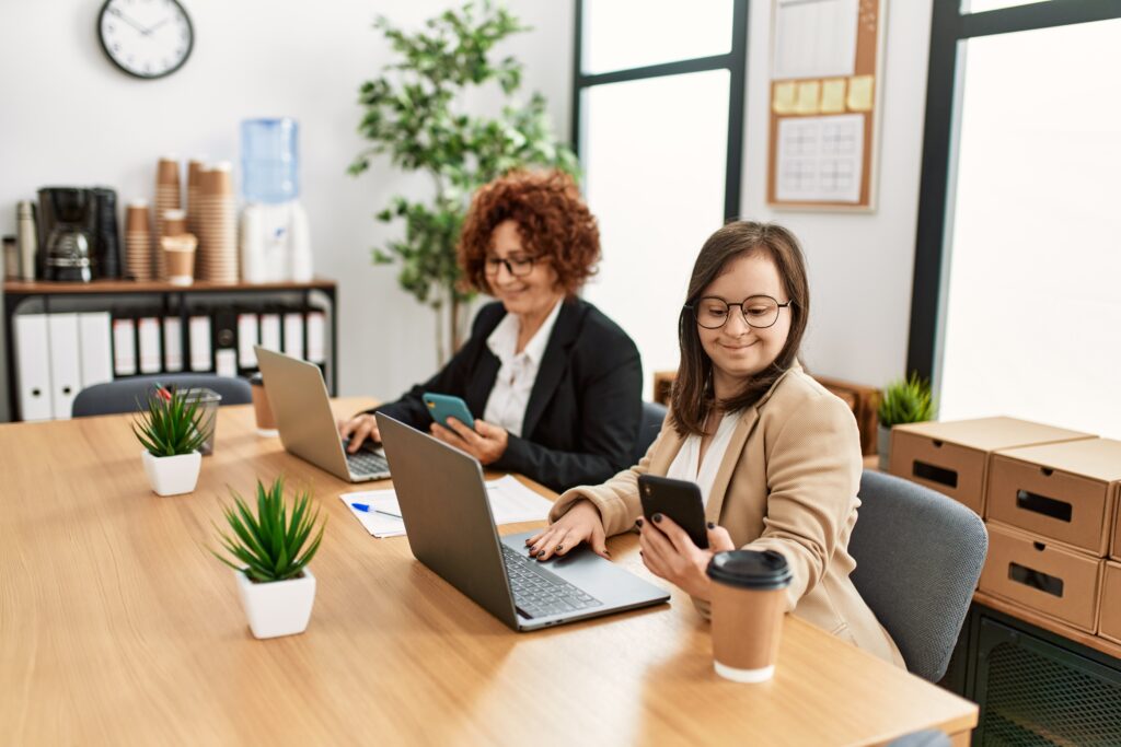 Group of two women working at the office. Mature woman and down syndrome girl working at inclusive teamwork.